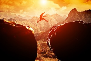 Man leaps across a precipice in the mountains at sunset.