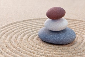 Photograph of three stones stacked in the center of a pattern raked into the sand of a Zen garden.