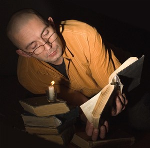 Photo of a man reading a book by candlelight.