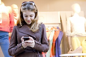 Photo of a young woman in a clothing store looking at her phone.