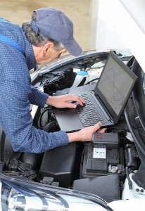 Man uses a laptop computer to examine a car engine.