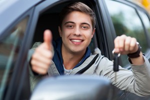 Photograph of smiling teen boy sitting in a car, flashing a key and a thumbs up. 