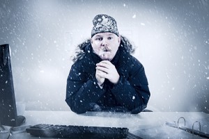 Photo of a man wearing a hat and parka, sitting at a desk in a snowstorm.